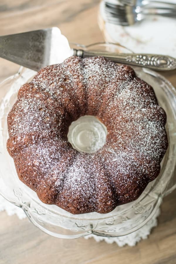 Butterscotch Poppy Seed Bundt Cake dusted with powdered sugar on a glass cake plate.
