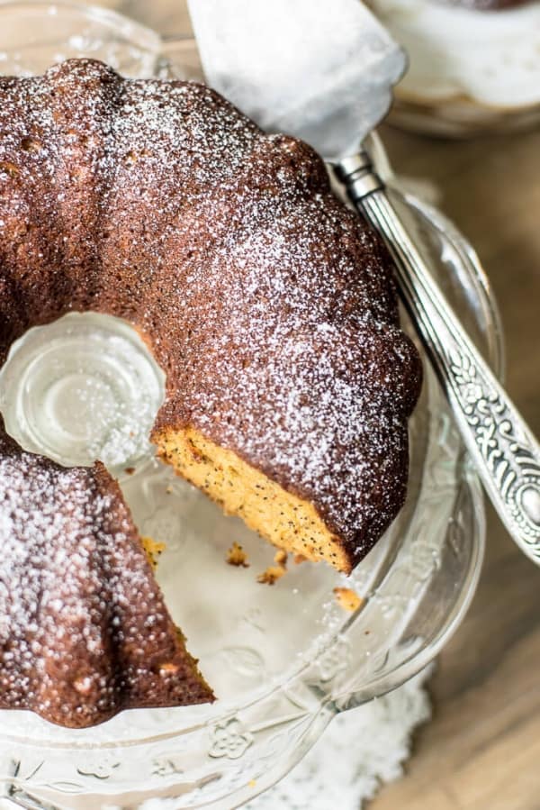 Butterscotch Poppy Seed Bundt Cake on a cake plate with a metal serving spatula.