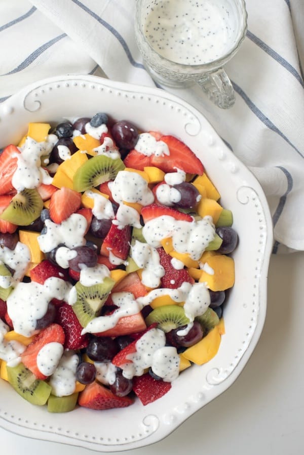 An over the top shot of the fruit salad in a white bowl with poppy seed dressing in the background.