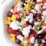 A bowl of fruit salad topped with poppy seed dressing.