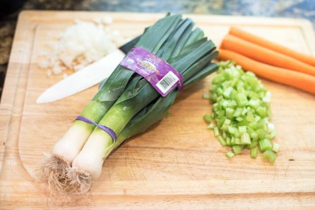 Leeks, carrots, onion, and celery on a cutting board.