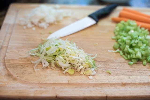 Sliced leeks on a cutting board with celery, carrots, and onion.