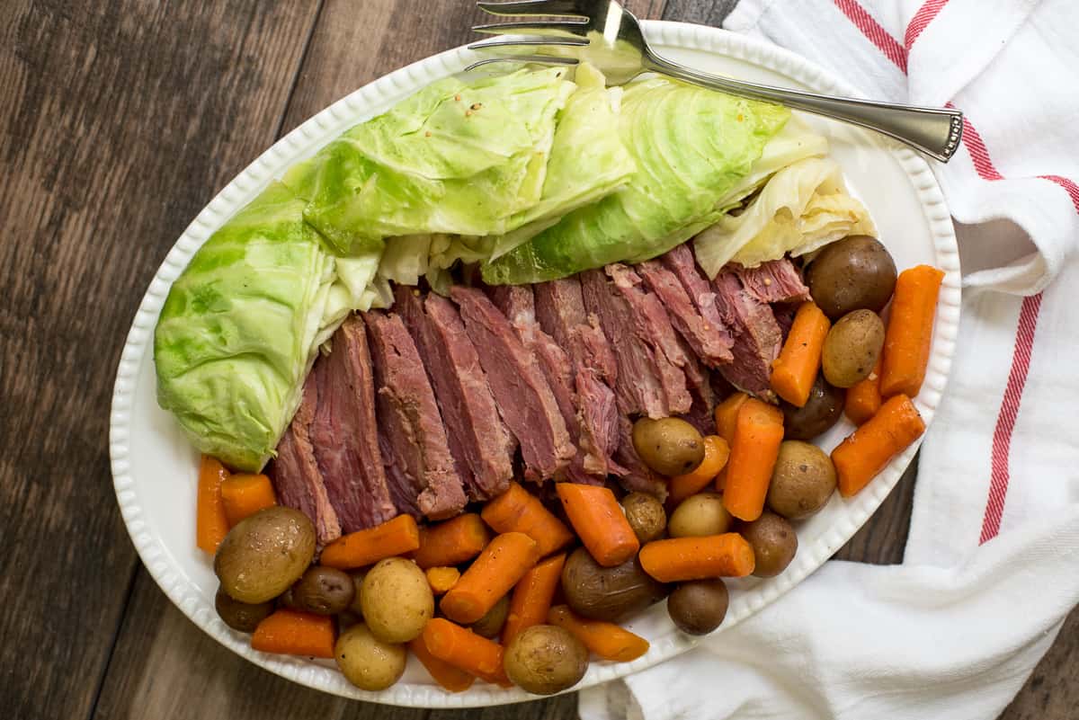 Sliced corned beef with cabbage, carrots and potatoes on a white platter.