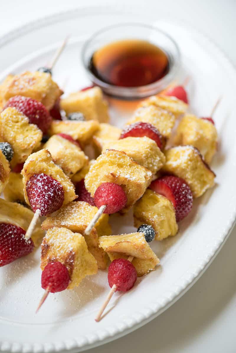 Berry French Toast Kabobs on a white plate with a small bowl of maple syrup.