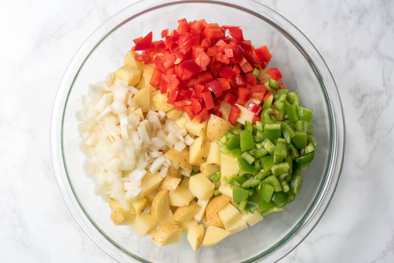 Red and green bell pepper, onion, and potatoes in a mixing bowl