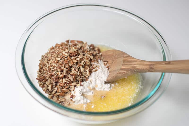 Dry ingredients are mixed into melted butter in a glass bowl.