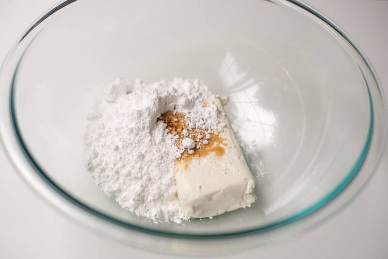 Cream cheese, powdered sugar and vanilla in a glass bowl.