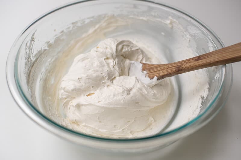 A wooden spoon stirs a creamy mixture in a glass bowl.
