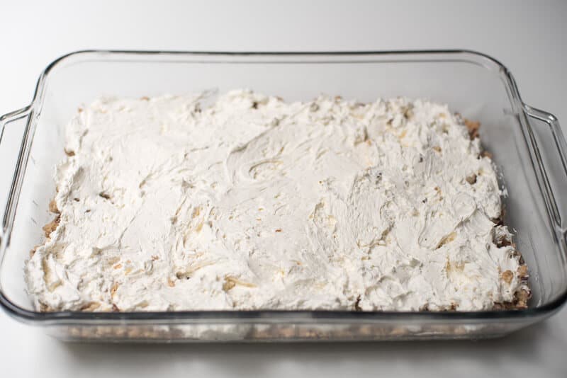 A creamy layer is spread out over a crust layer in a glass dish.