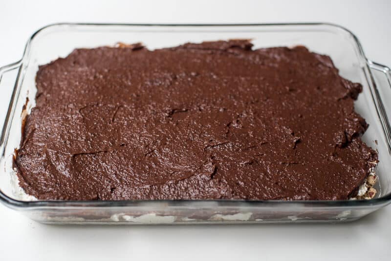 A chocolate pudding mixture is spread out on top of a creamy layer in a glass dish.