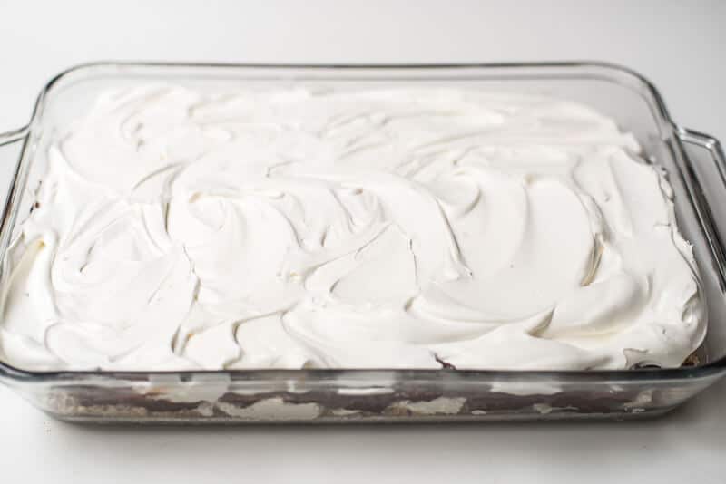 Cool Whip is layered over a dessert in a glass dish.