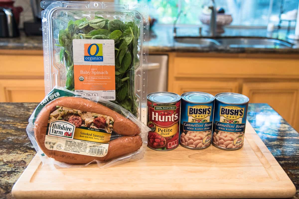 Smoked sausage, baby spinach, canned white beans, and diced tomatoes on a kitchen counter.