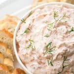 A bowl of salmon dip with slices of bread around it.