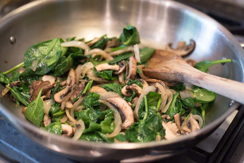 Spinach, mushrooms, and onions cooking in a skillet.