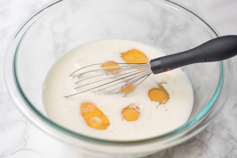 Milk and eggs in a bowl with a whisk.