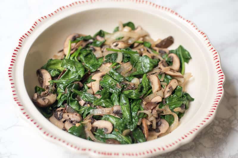 Spinach, mushrooms, and onions in a round pie dish.