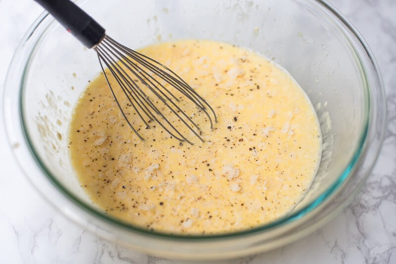 An egg mixture in a bowl with a whisk.
