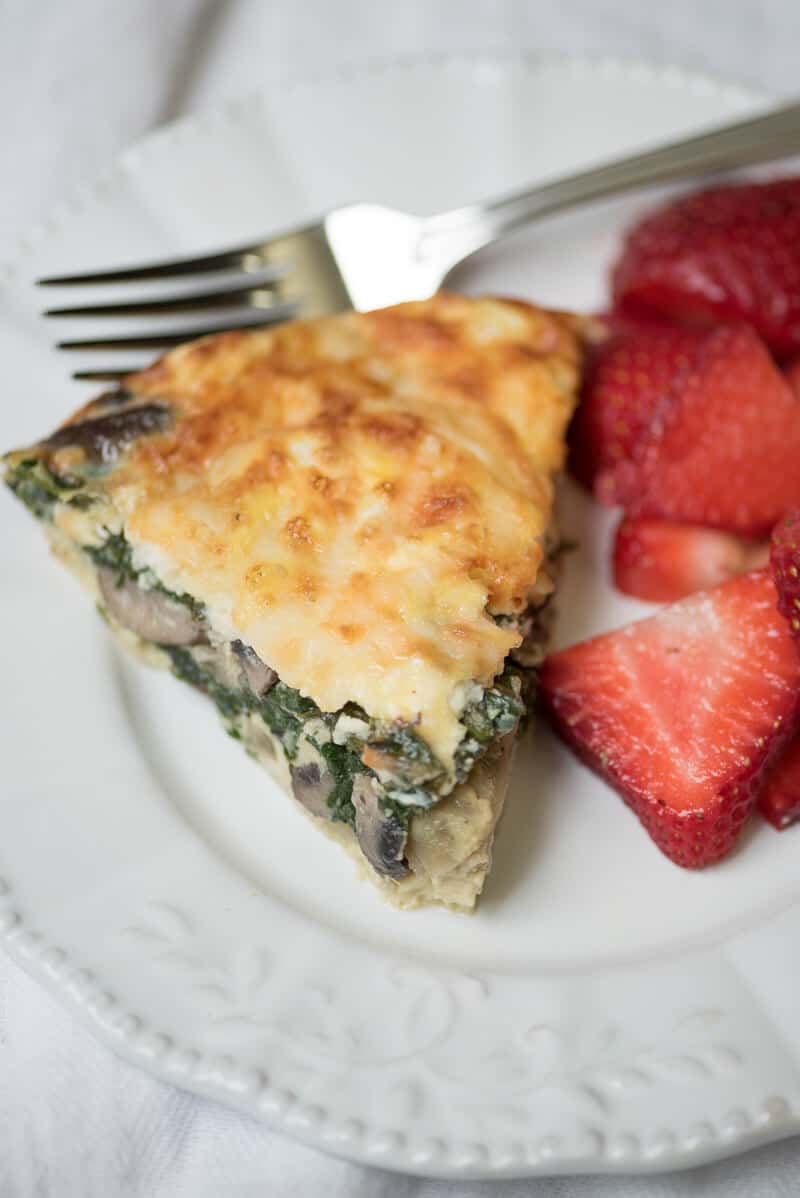 A slice of quiche on a plate with strawberries and a fork.