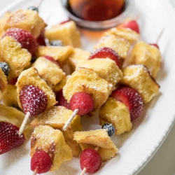 Skewers of french toast cubes and berries stacked on a plate.