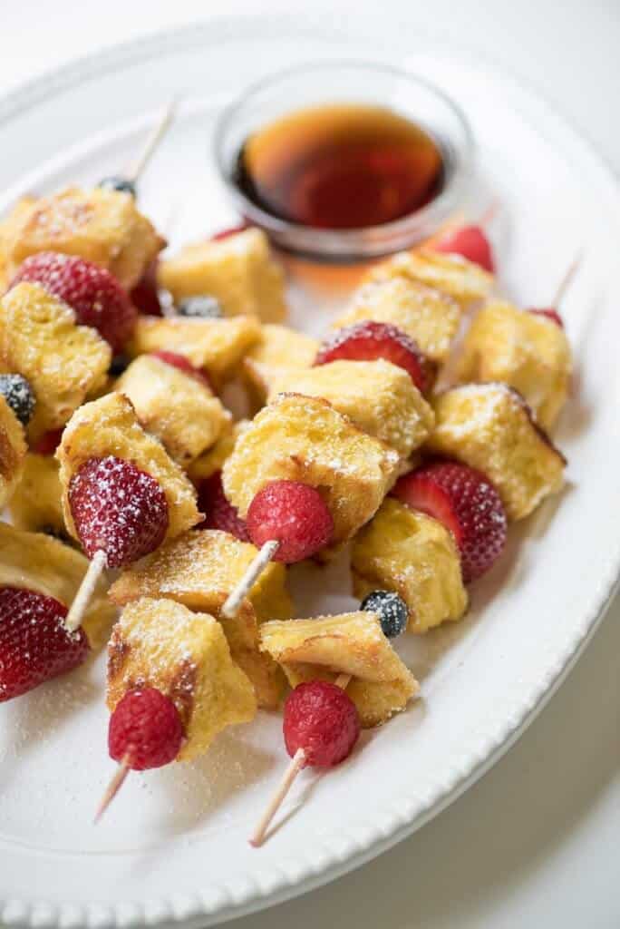 Skewers of french toast cubes and berries stacked on a plate.