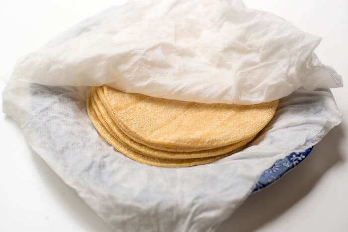 A stack of corn tortillas on a plate between wet paper towels.