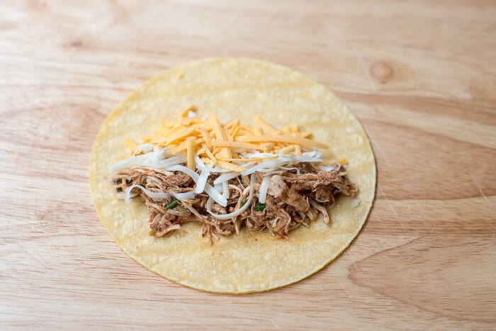 A corn tortilla on a cutting board with some of the shredded chicken and cheese.