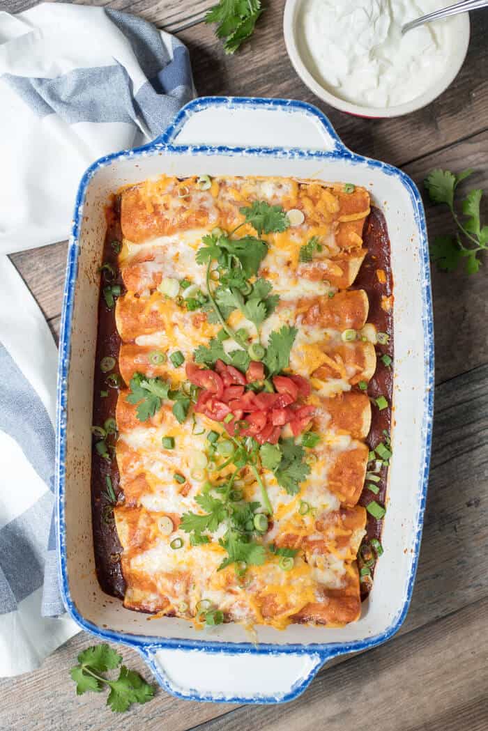 An over the top image of Easy Slow Cooker Chicken Enchiladas in a white casserole dish with a bowl of sour cream.