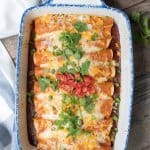 A baking dish full of enchiladas topped with cilantro and tomato.