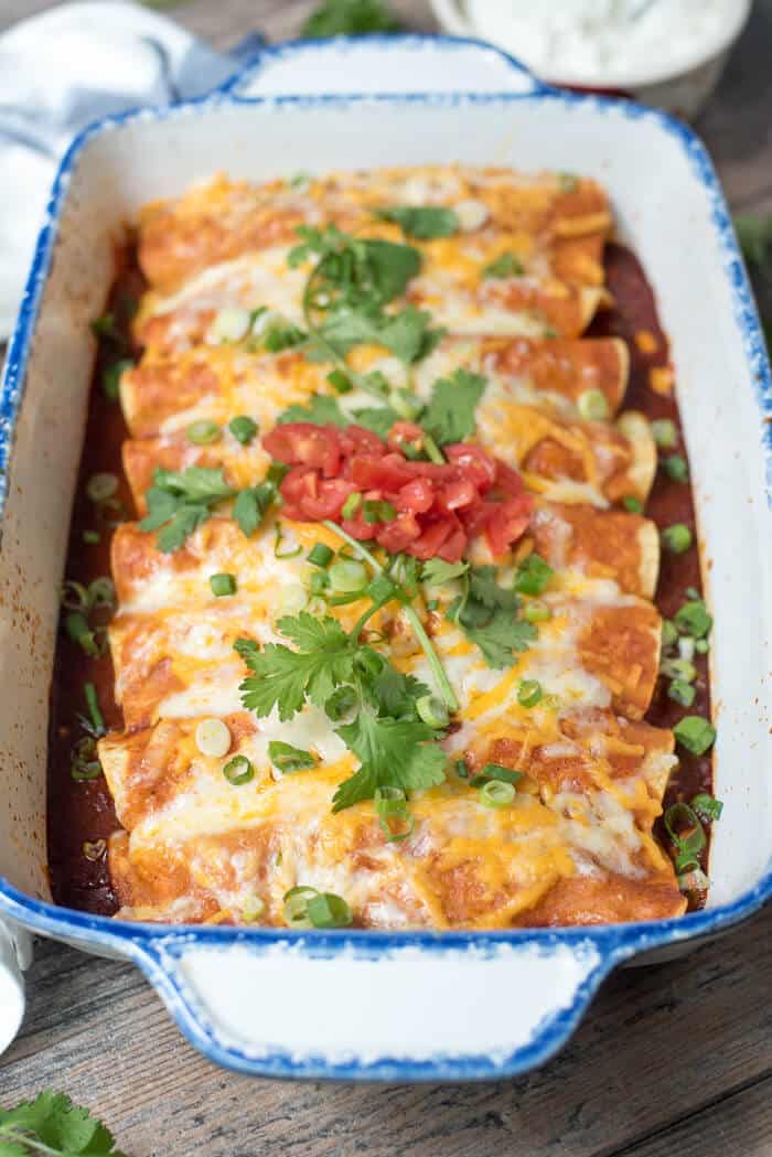 Enchiladas in a white casserole dish topped with cilantro and tomatoes.