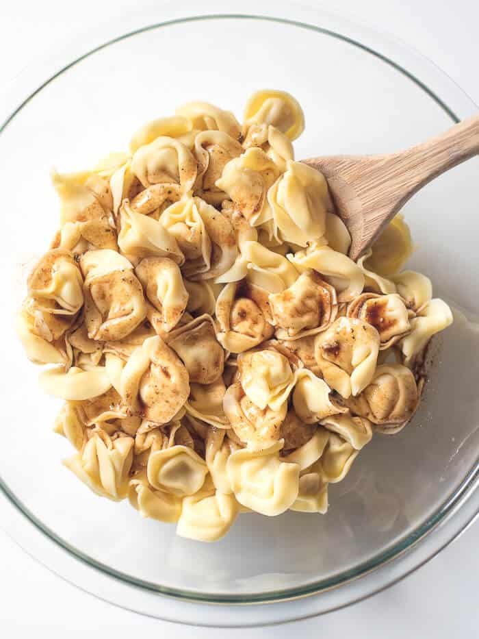 Dressing being stirred into cheese tortellini with a wooden spoon.