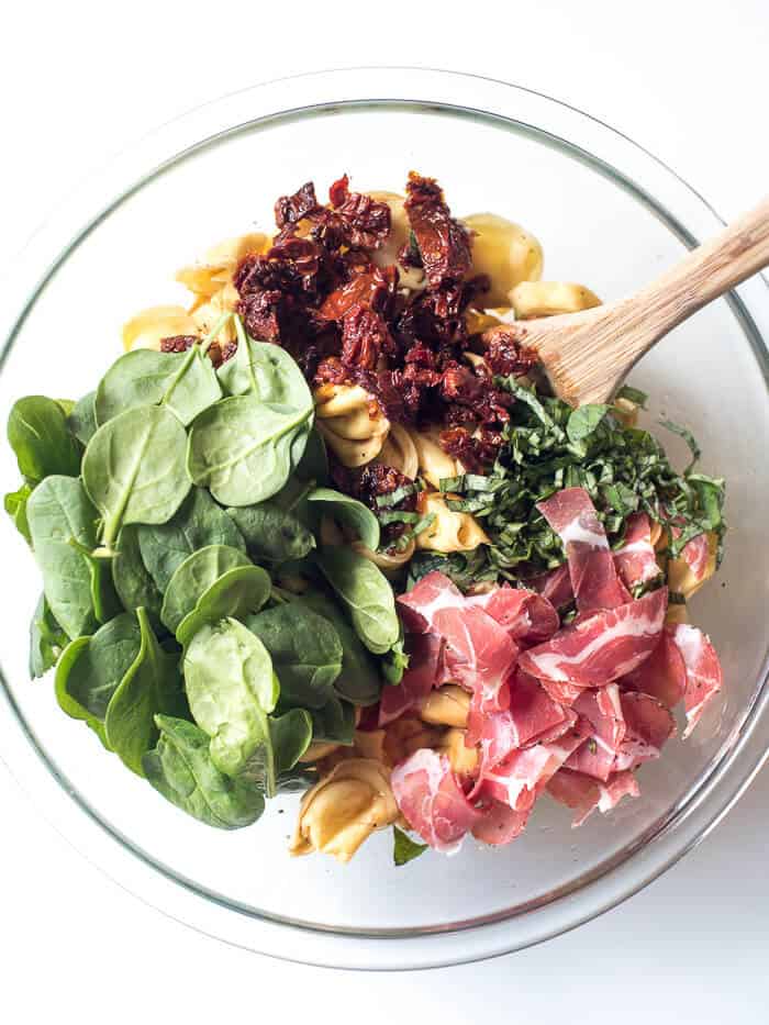 Tortellini, sundried tomatoes, coppa, and spinach in a bowl.