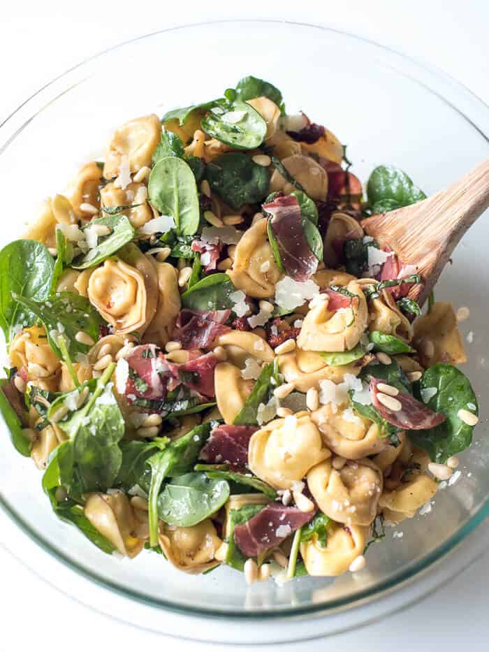 Italian Tortellini Salad in a glass bowl with a wooden spoon.