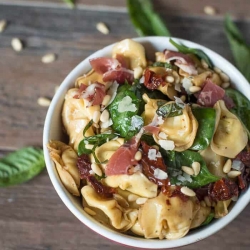 A small white bowl filled with tortellini, spinach, and coppa.