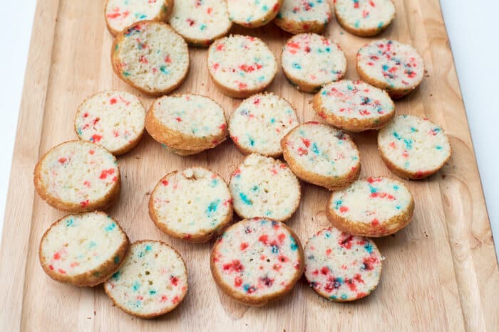 The funfetti cupcakes sliced in half on a cutting board.