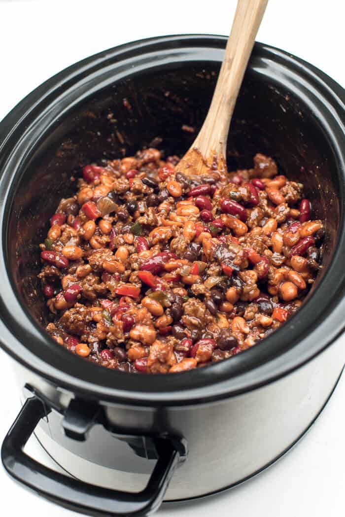 A wooden spoon stirs the beans in the slow cooker.