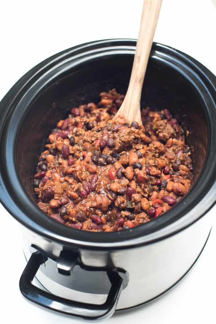 A wooden spoon scoops up some of the 3-Bean Cowboy Beans from the slow cooker.