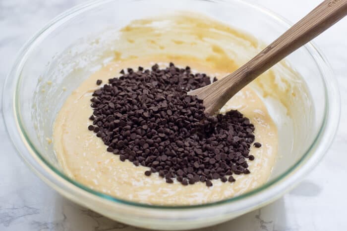 Mini chocolate chips are stirred into the batter with a wooden spoon.