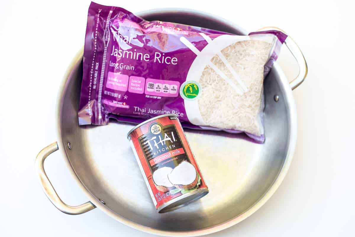 A package of Jasmine Rice and a can of Thai Kitchen Coconut Milk in a stainless steel skillet.