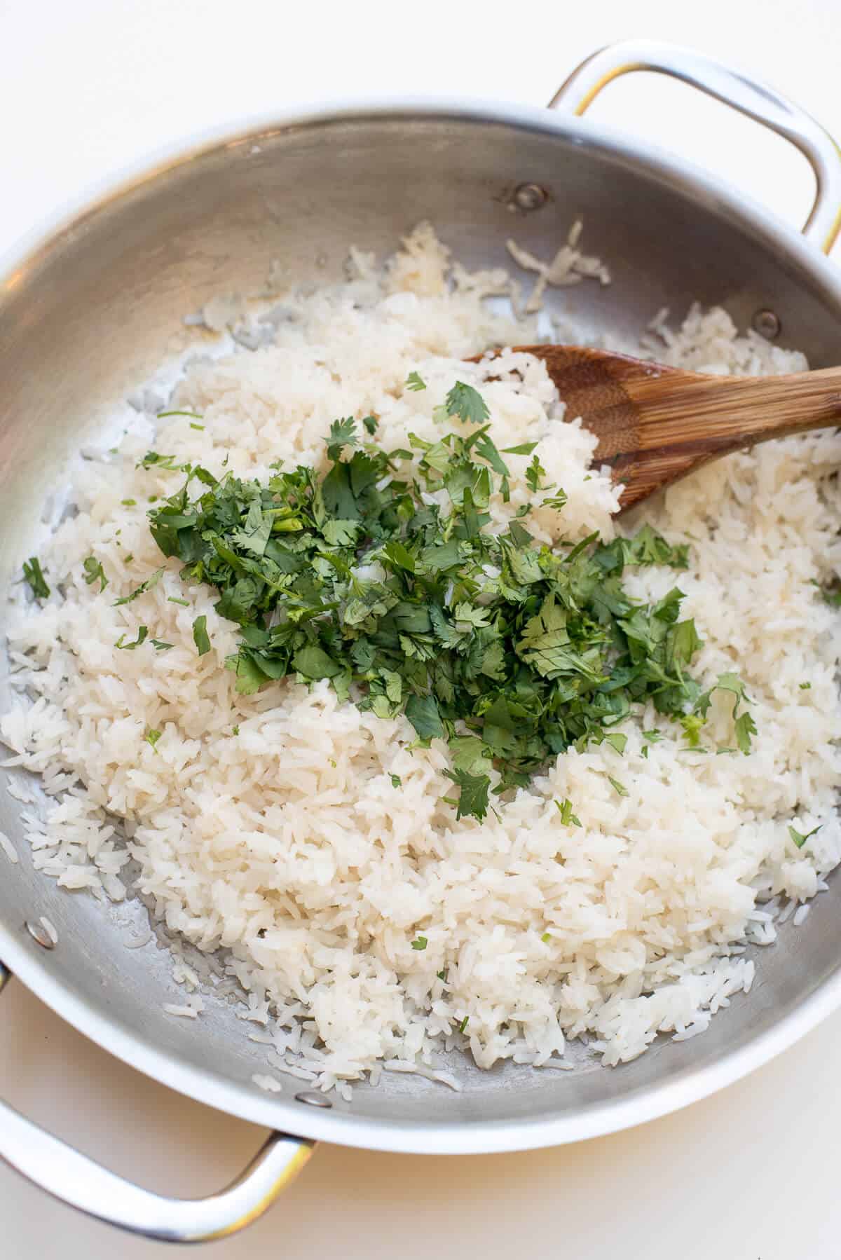 Cilantro is stirred into rice in a stainless steel skillet.