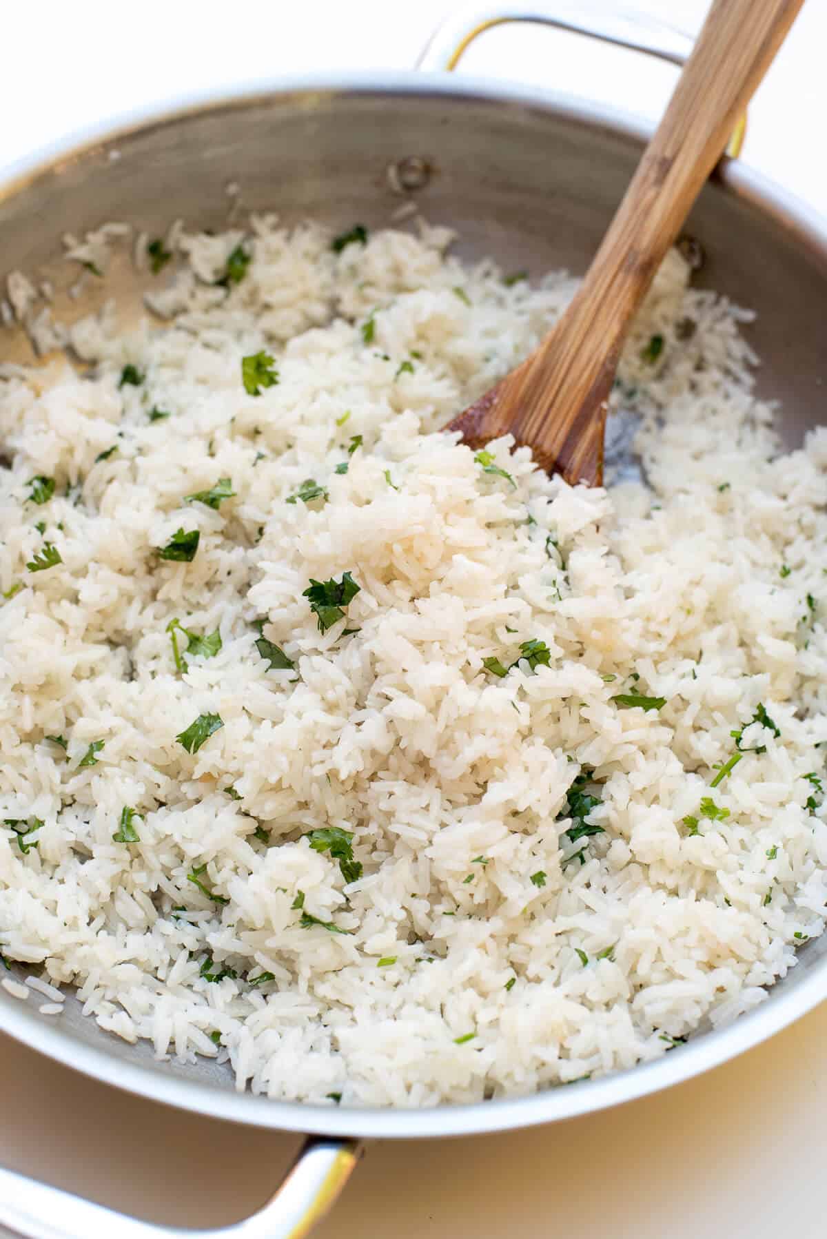 A wood spoon stirs the cilantro into the rice in the skillet.