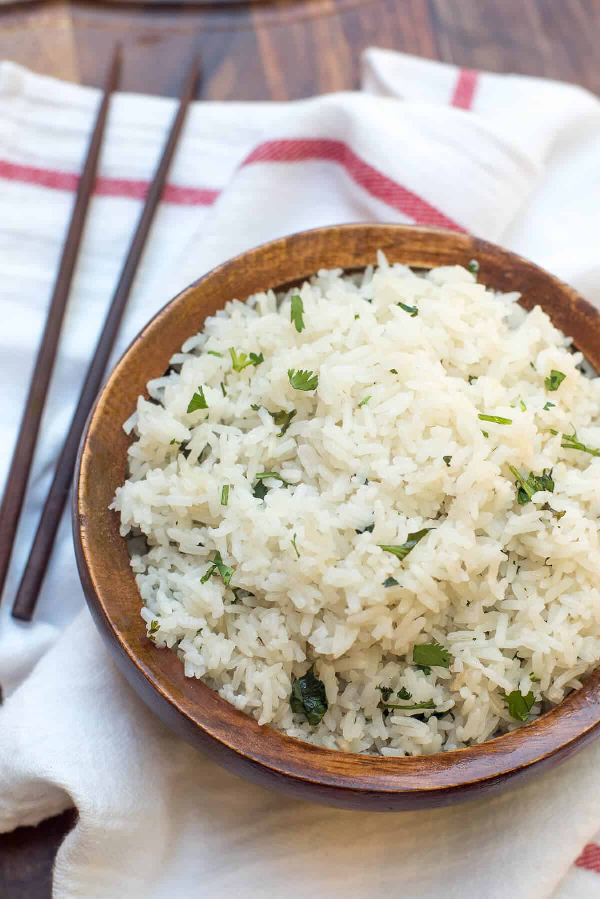 A wooden bowl filled with Coconut Rice with chopsticks lying next to it.