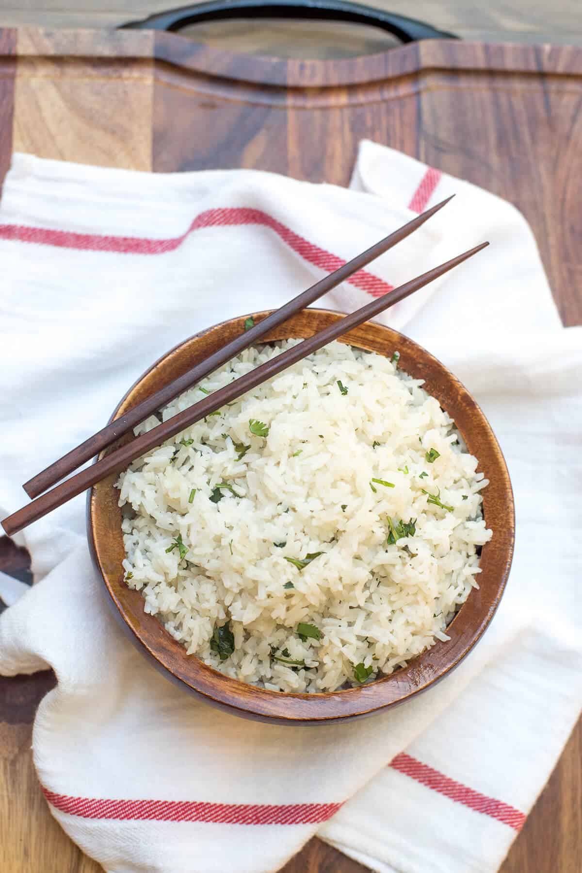 An over the top image of a wooden bowl filled with Coconut Rice with chopsticks lying over the top.