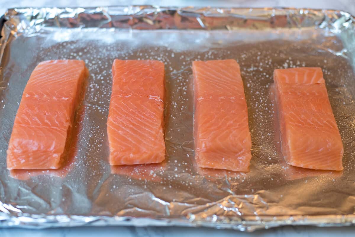 Salmon fillets on a foil lined baking sheet seasoned with salt.