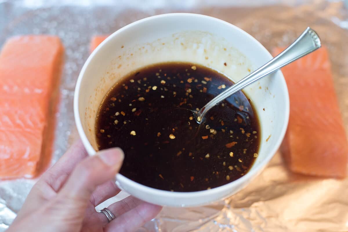 A hand holding Orange Sesame Ginger Glaze in a white bowl.