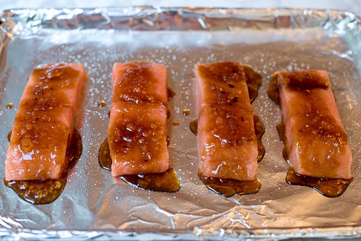 Salmon fillets on a foil lined baking sheet topped with Orange Sesame Ginger Glaze.