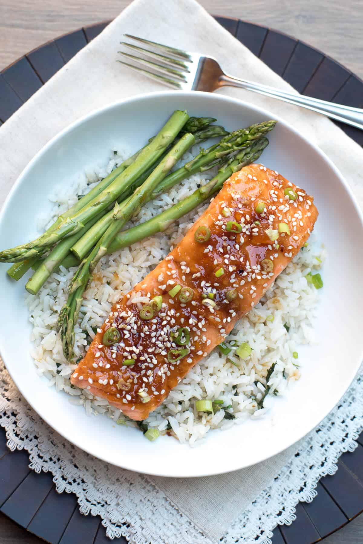 Orange Sesame Ginger Glazed Salmon on a bed of white rice with asparagus in a white bowl with a fork.