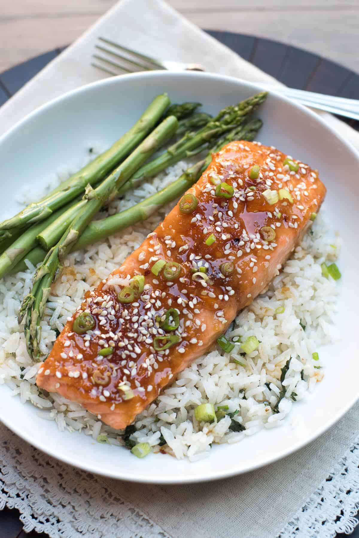 Orange glazed salmon on a bed of rice next to asparagus in a bowl.