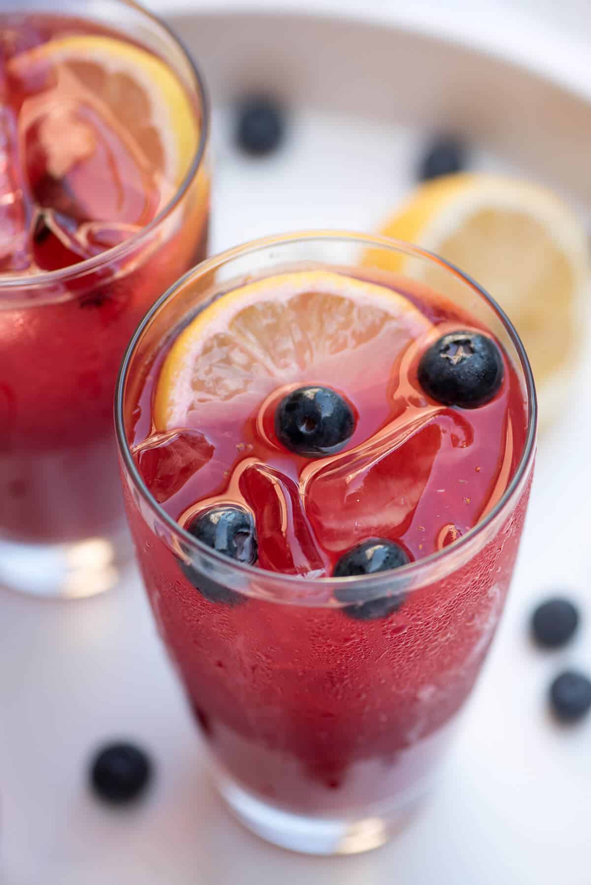 A closeup shot down shot of a glass of Berry Lemonade with ice, berries, and a lemon slice.