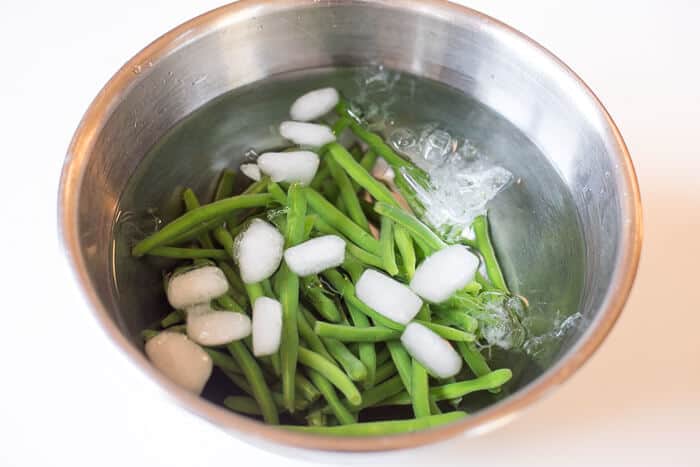 Green beans in a metal bowl filled with ice water.