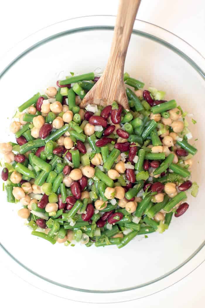 An over the top image of the Three Bean Salad in a glass bowl with a wooden spoon.